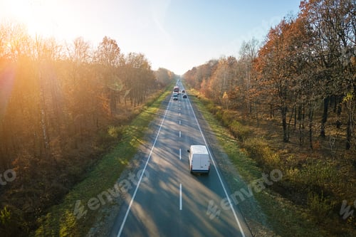 Preview: Aerial view of intercity road with fast driving cars between autumn forest trees at sunset.