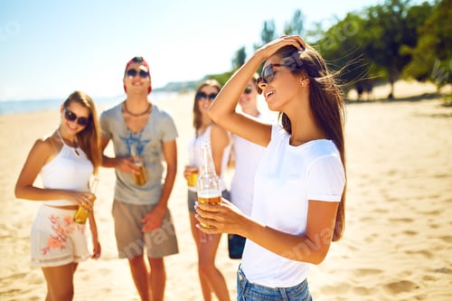 Preview: Smiling young girl with beer. other while people barbecuing in the background. Fun at the beach.