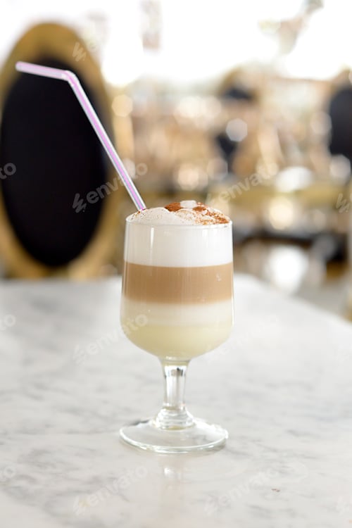 Preview: transparent glass with latte coffee with syrup and milk,poured in lines,with lush foam,cinnamon