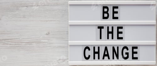 Preview: 'Be the change' words on a modern board on a white wooden surface, top view.