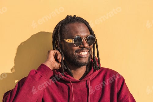 Preview: Smiling black man in sunglasses and dreadlocks looking away on yellow background