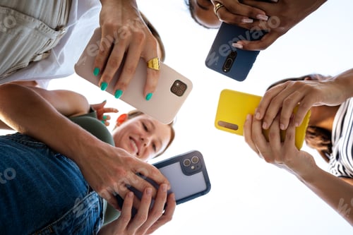 Preview: Low angle view of four female friends using phone in a circle. Focus on phones and hands.