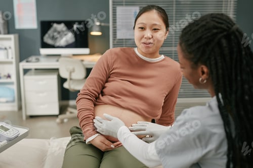 Preview: Pregnant Young Adult Asian Woman Undergoing Abdominal Exam by Black Doctor