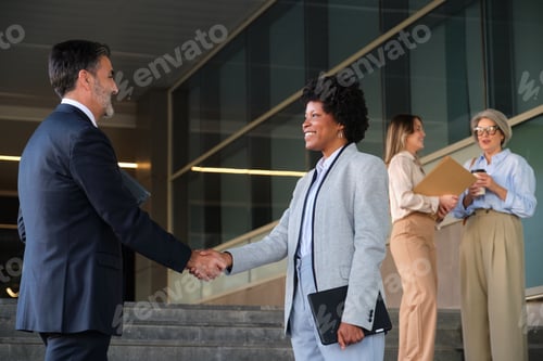 Preview: Businesspeople shaking hands in front of modern office building