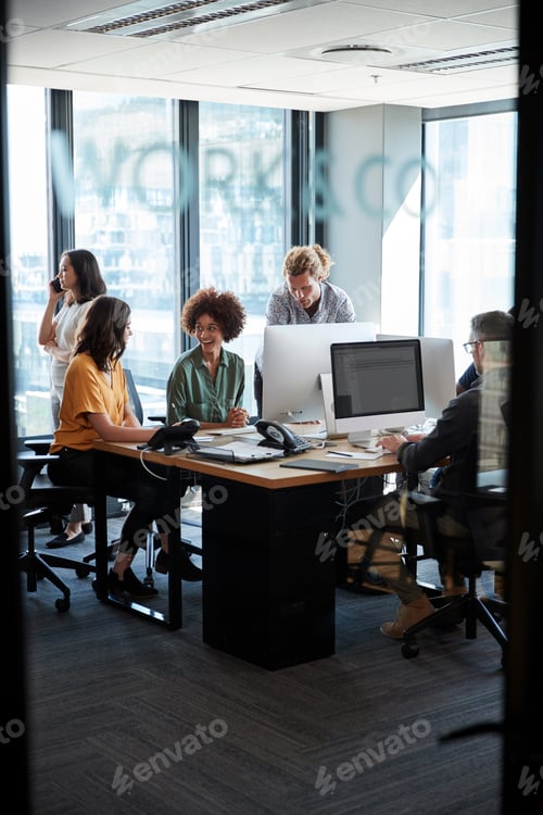 Preview: Creative colleagues in working in a casual office, seen through glass wall with text on it, vertical