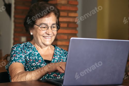 Preview: Senior woman with glasses using a laptop at home