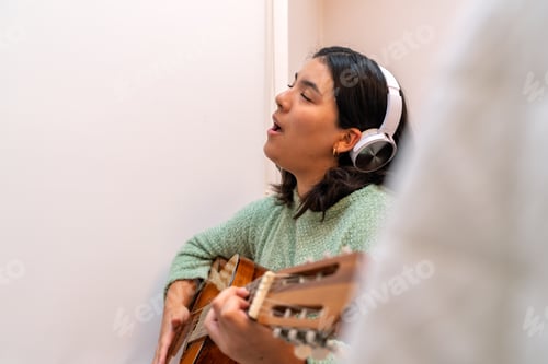 Preview: Singer songwriter composing new music playing acoustic guitar and wearing headphones at home
