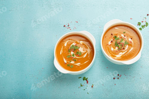 Preview: Two bowls of creamy pumpkin soup decorated with parsley and pepper on blue background top view copy
