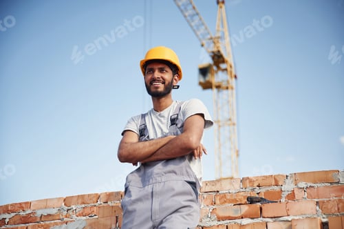 Preview: Standing with arms crossed. Handsome Indian man is on the construction site