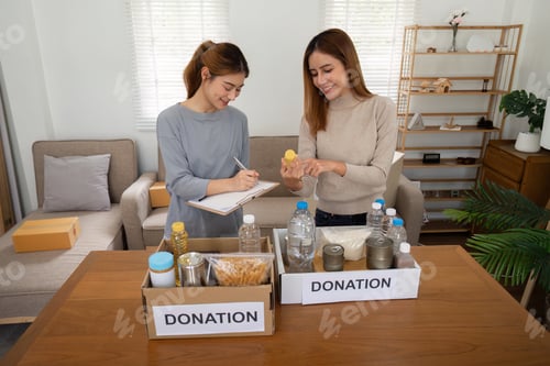 Preview: Donation and two woman volunteer asian of happy packing food in box at home. Charity