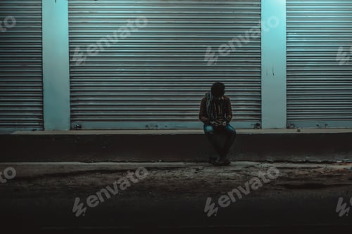 Preview: Lonely man sitting on the concrete surface against lighted wall background
