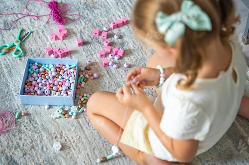 Preview: Little girl making wooden beads bracelet at home living room. Children's creativity and the