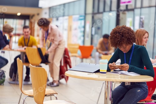 Preview: Communal Area Of Busy College Campus With Female Student Working At Tables And Using Mobile Phone