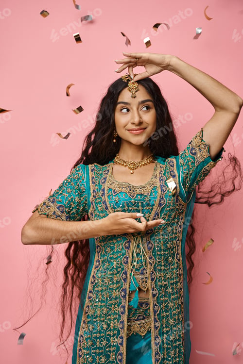 Preview: jolly attractive indian woman gesturing and looking away under confetti rain on pink backdrop