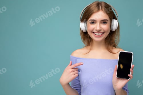 Preview: Attractive happy young blond woman wearing blue crop top isolated over blue background wall holding