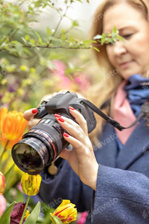 Preview: A young woman takes a photo on camera of tulips in a spring blooming garden. Blossom