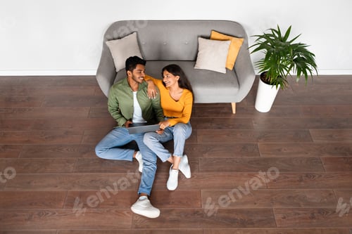 Preview: Indian couple smiling, websurfing on floor with laptop