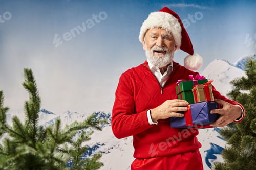 Preview: white bearded cheerful Santa holding present pile with snowy mountain backdrop, winter concept
