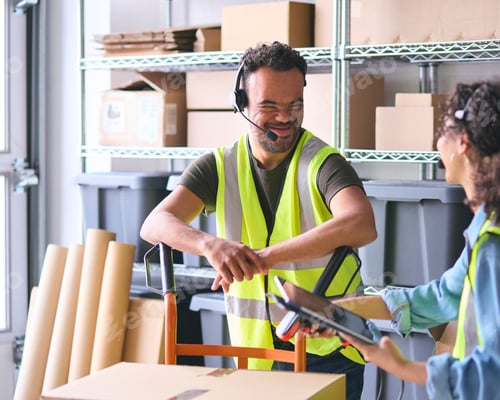 Preview: Woman Using Digital Tablet And Male Colleague With Down Syndrome In Warehouse Wearing Headsets