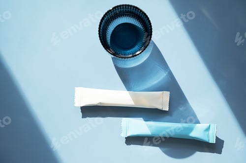 Preview: White and blue collagen supplement sticks with glass of water.