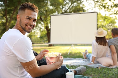 Preview: Young man with popcorn watching movie in open air cinema. Space for text