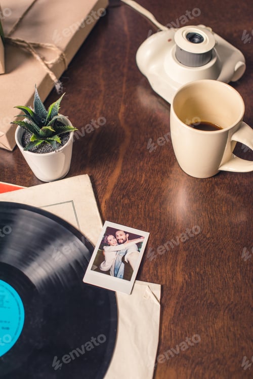 Preview: Composition of vynil record and instant photo, camera and coffe cup on table