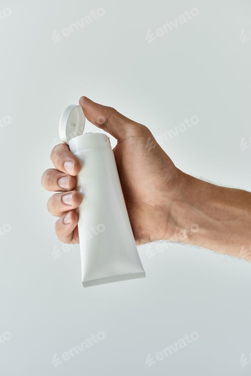 Preview: Young man holding beauty product against a simple grey backdrop