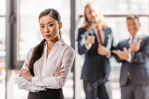 Preview: asian businesswoman with crossed arms, businessmen standing behind and laughing