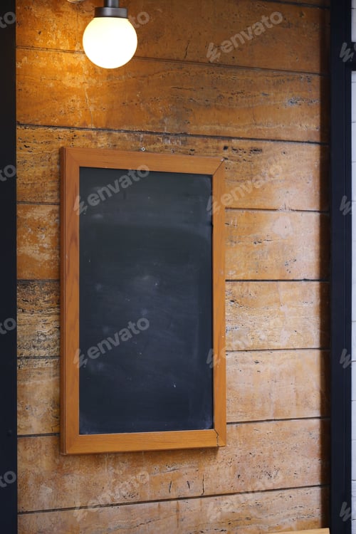 Preview: Empty chalkboard on wooden wall with warm light above