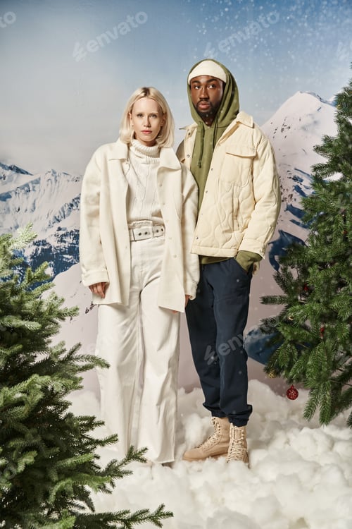 Preview: attractive diverse couple posing together in winter warm attire with snowy backdrop, fashion concept