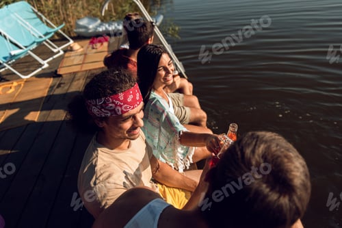 Preview: Group of friends sitting on the edge of a pier having fun and enjoying a summer day at the lake.