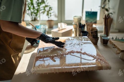 Preview: Closeup of female artist applying epoxy resin with gloved fingers in art studio closeup. Fluid art.