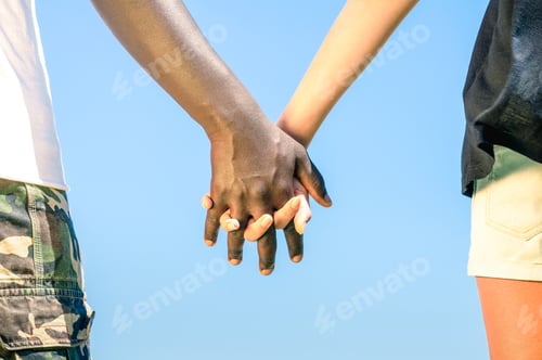 Preview: Multiracial couple walking hand in hand against a blue sky