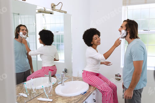 Preview: Diverse couple standing in bathroom applying shaving cream