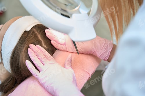 Preview: Woman checks client head while looking through loupe lamp