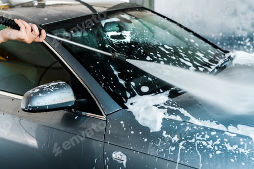 Preview: cropped view of car cleaner holding pressure washer with water near automobile