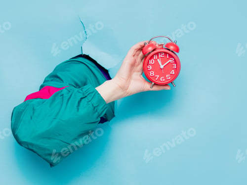 Preview: Female hand in 90s style jacket holding alarm clock
