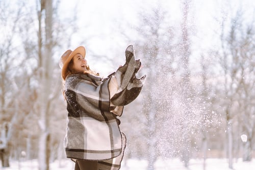 Preview: Beautiful woman standing among snowy trees and enjoying first snow. Happy winter time. Christmas.