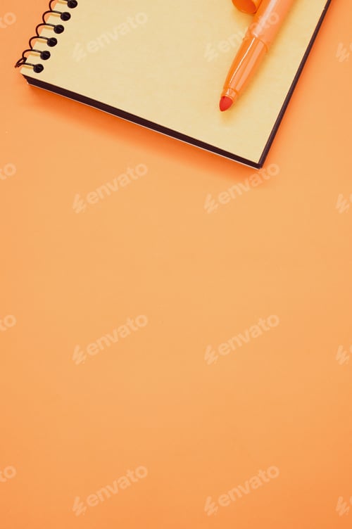 Preview: Vertical shot of a notebook and an orange marker on an orange surface