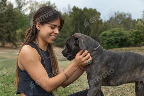 Vista lateral de una dueña positiva con pelo largo acariciando a un adorable perro mastín italiano negro mientras