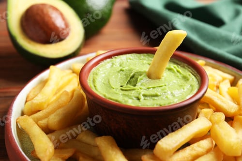 Preview: Plate with french fries, guacamole dip and avocado served on wooden table, closeup