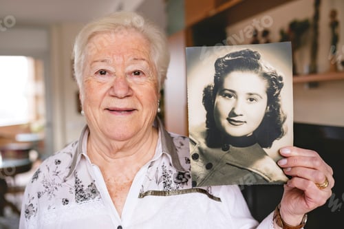 Preview: Portrait of senior woman showing an old picture of herself