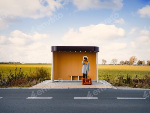 Preview: Woman in coat with suitcase and binocular on countryside bus stop