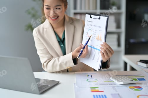Preview: Focused asian businesswoman explaining charts during video call, immersed in data analysis with lapt