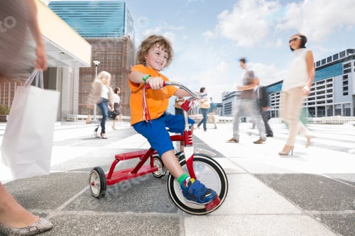 Preview: Boy riding a tricycle between a crowd of people in a city