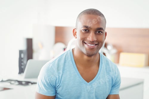 Preview: African American man sitting while smiling at countertop in home kitchen, using laptop and speaker