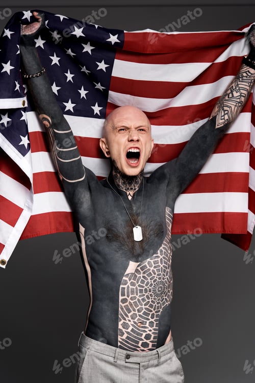 Preview: excited shirtless bare-chested man with tattoos holding american flag and screaming isolated on grey