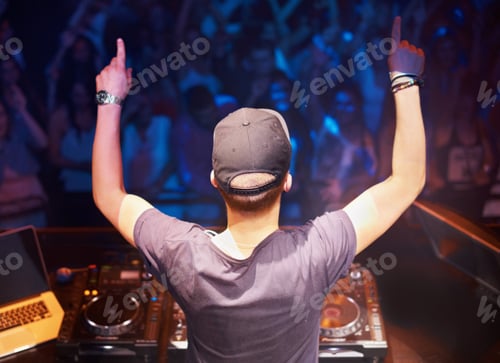Preview: Rear view of a dj standing behind the decks with his hands in the air