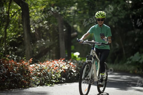Preview: Woman cyclist using smartphone while riding bike on sunny day