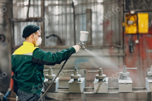 Preview: Powder primer coating of metal parts. Worker man in a protective suit sprays powder paint from gun